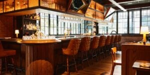 Wood-paneled bar with tufted leather stools, hanging wine glasses, and exposed brick at Little West Tavern, Columbus