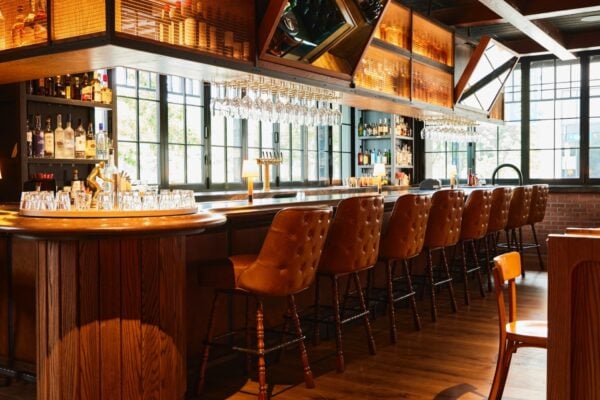 Wood-paneled bar with tufted leather stools, hanging wine glasses, and exposed brick at Little West Tavern, Columbus