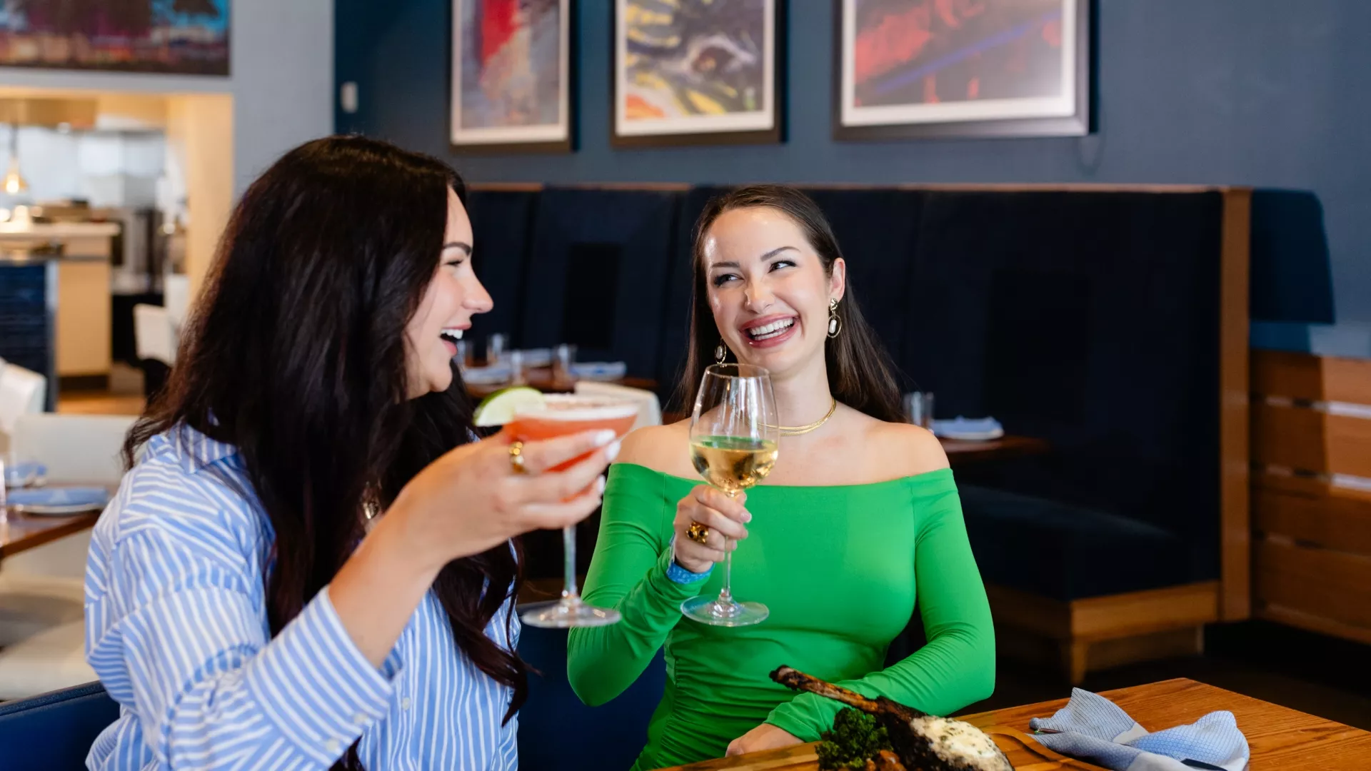 Two women laughing and toasting with a pink cocktail and white wine at a restaurant table at Margaritaville Hotel Nashville